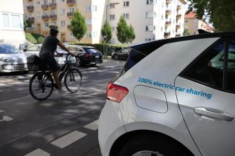 Ein Elektroauto steht am Straßenrand, ein Fahrradfahrer fährt vorbei.