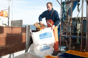 Ein Fischer packt Meeresmüll in einen Fishing-for-Litter-Müllsack.