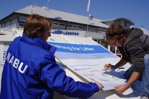 NABU-Vertreter und Fischereivertreter bringen ein Plakat auf einem Boot an.